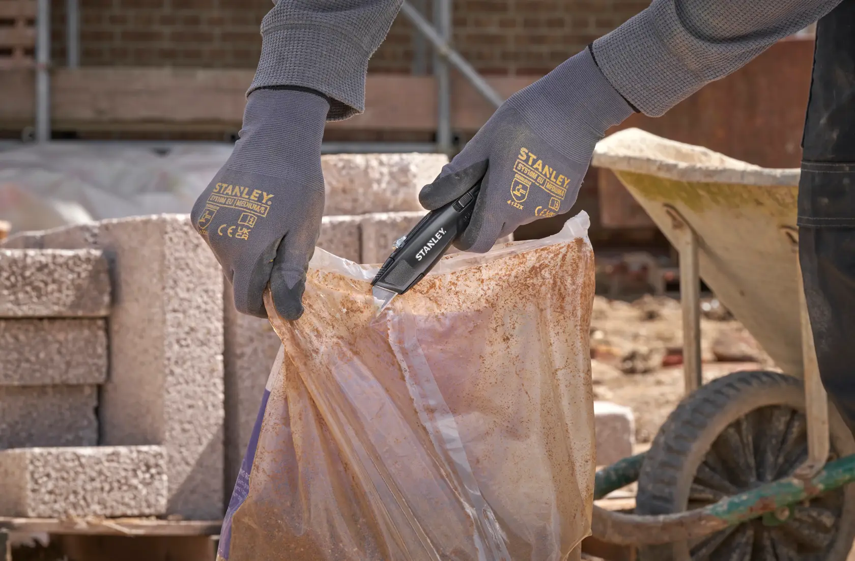 Photo d'un travailleur utilisant le couteau utilitaire STANLEY FMHT10504-0 pour ouvrir un sac plastique sur un chantier.