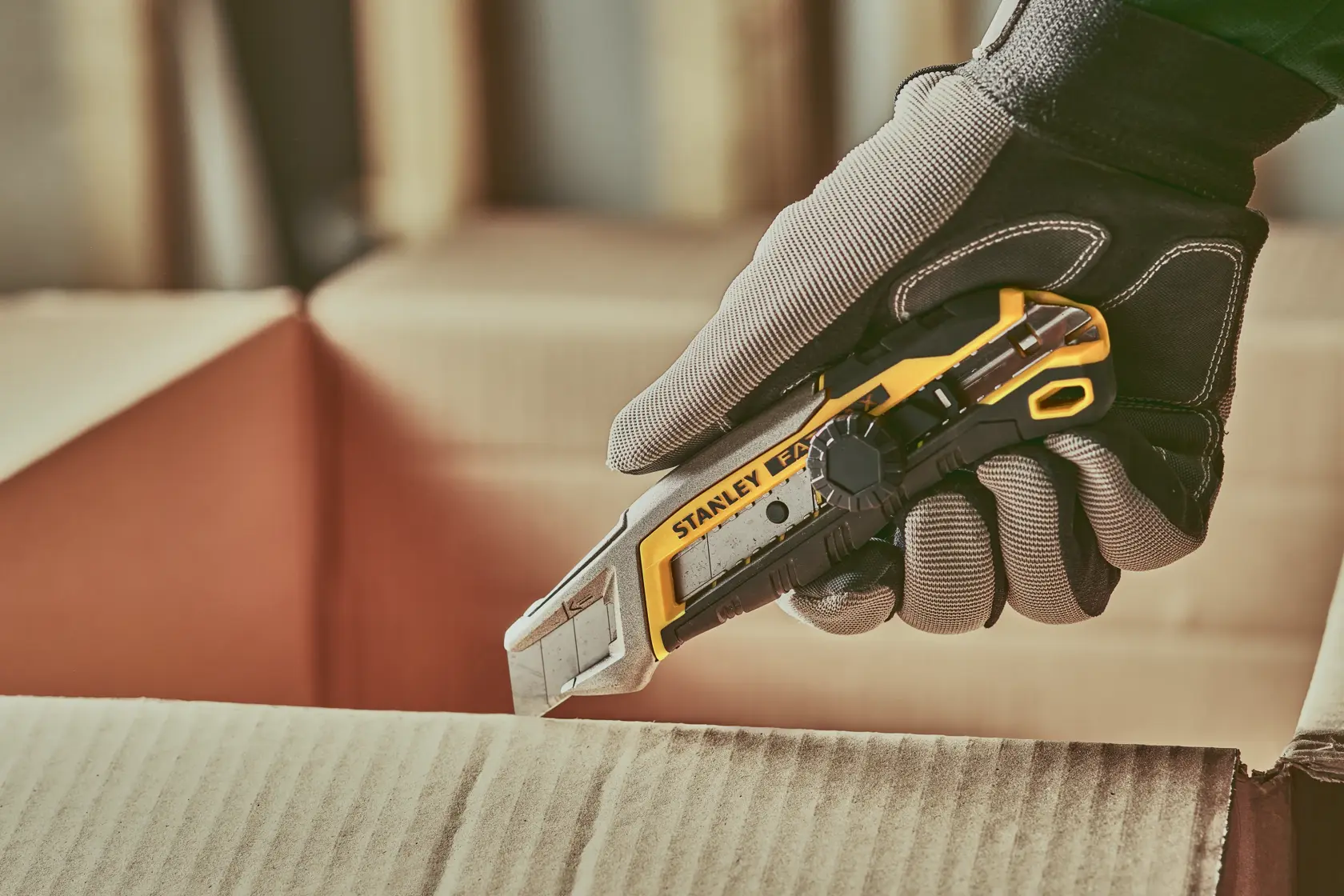 Stanley FATMAX utility knife, angled side view, silver and yellow body with black grip and blade exposed