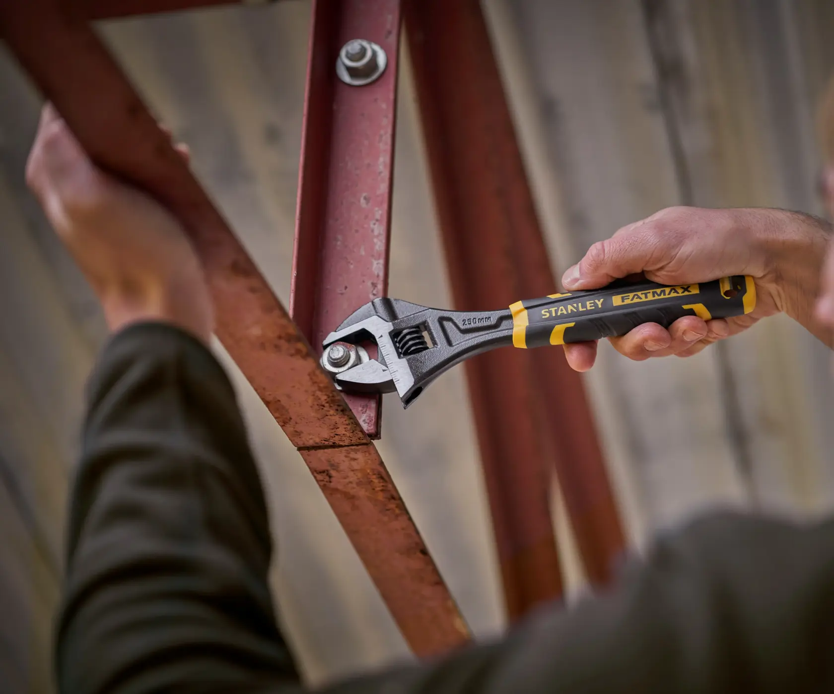 Stanley adjustable wrench being used to tighten a bolt on a red metal frame.