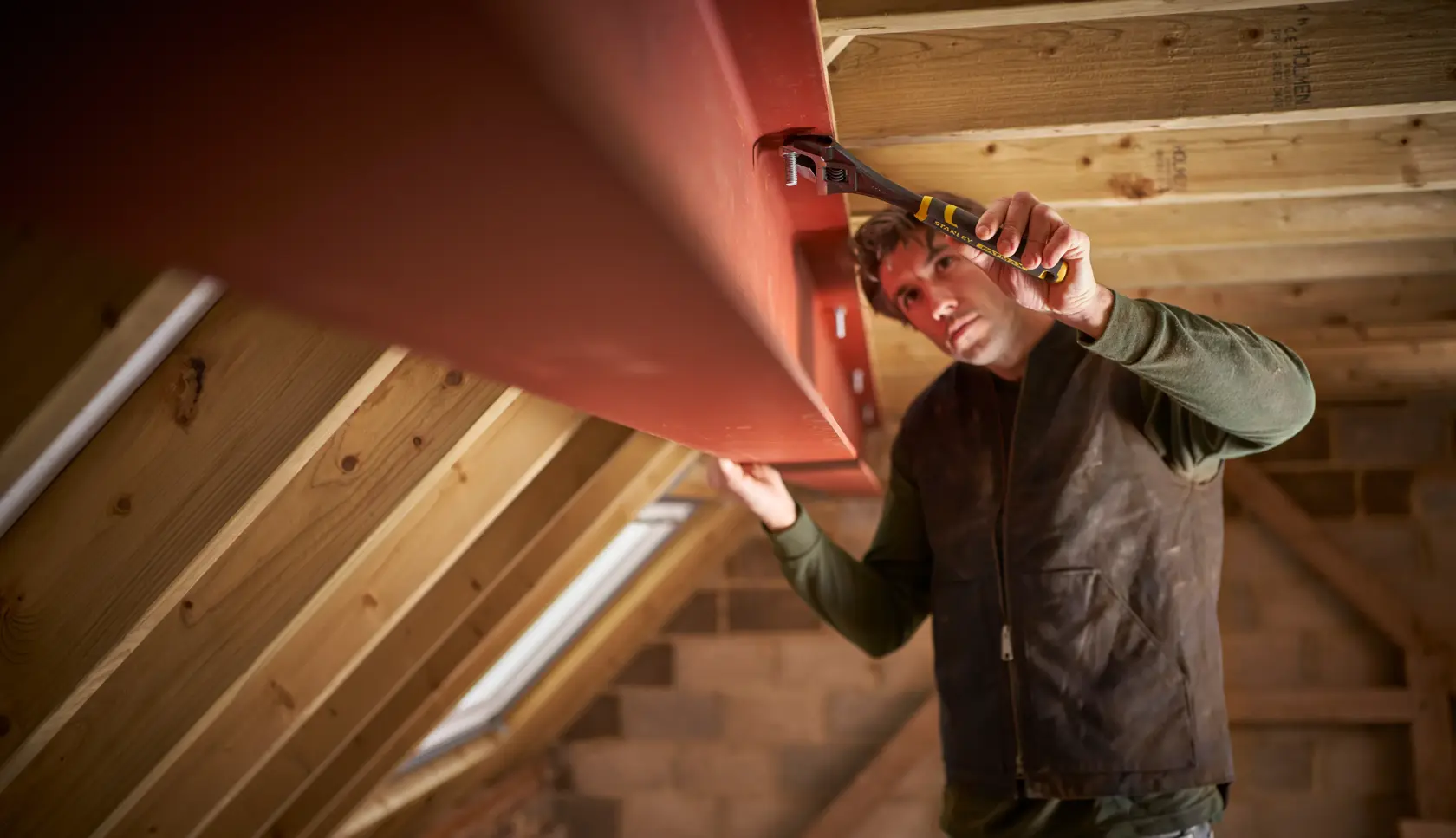 STANLEY FMHT13125-0 pliers used to grip metal beam in attic construction setting, side angle.