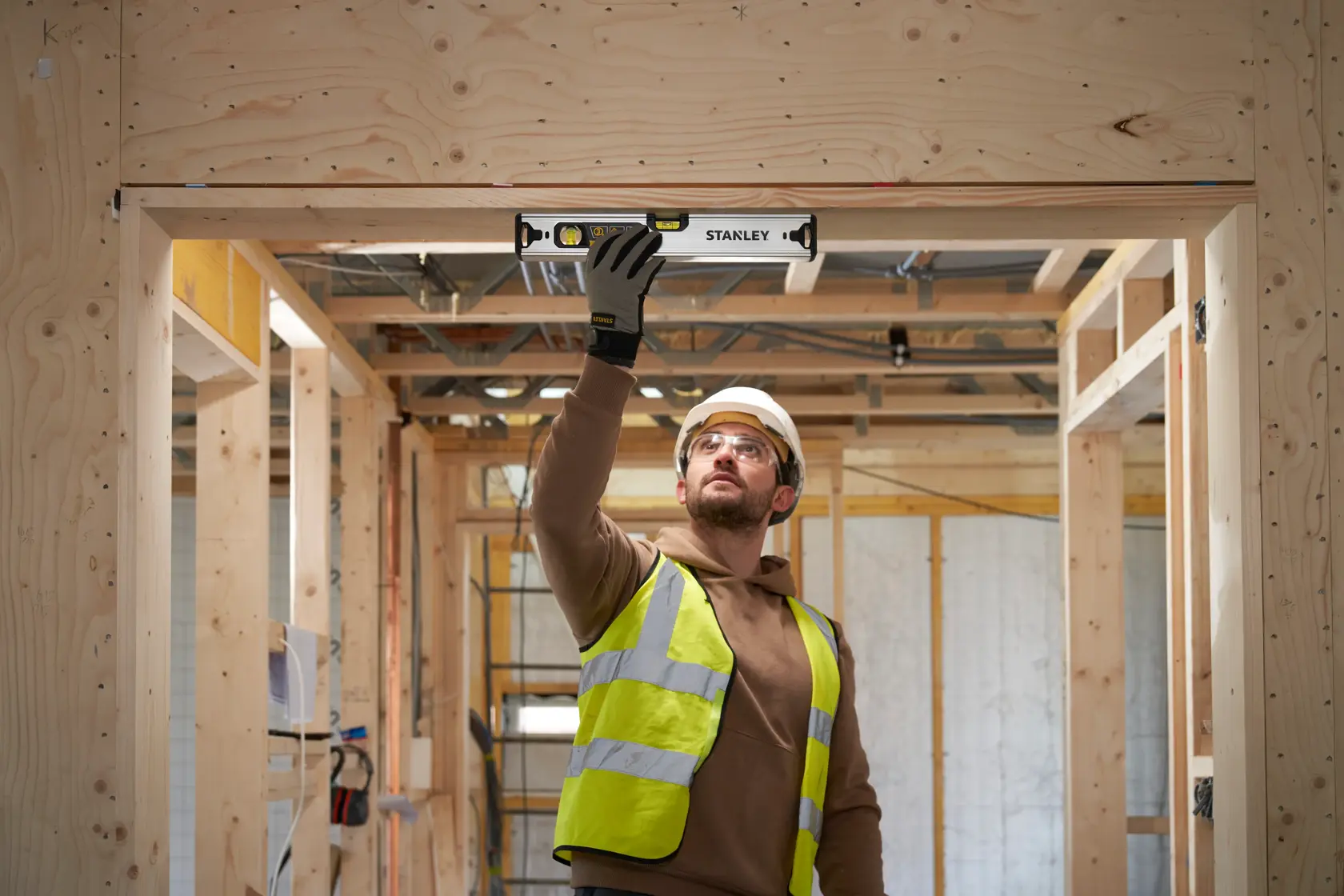 Photo of a worker using a STANLEY FMHT43670-1 spirit level on a wooden door frame at a construction site.