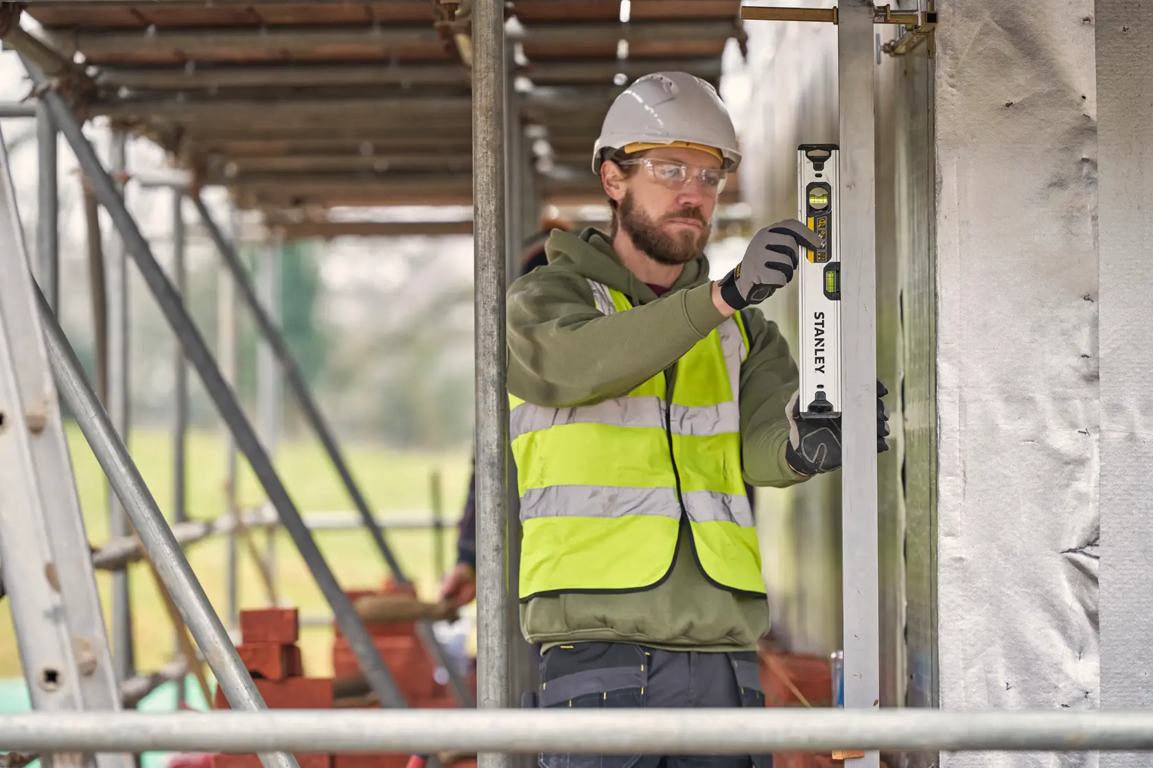 Photo of worker using STANLEY FMHT43671-1 spirit level on construction site, wearing hi-vis vest and helmet.