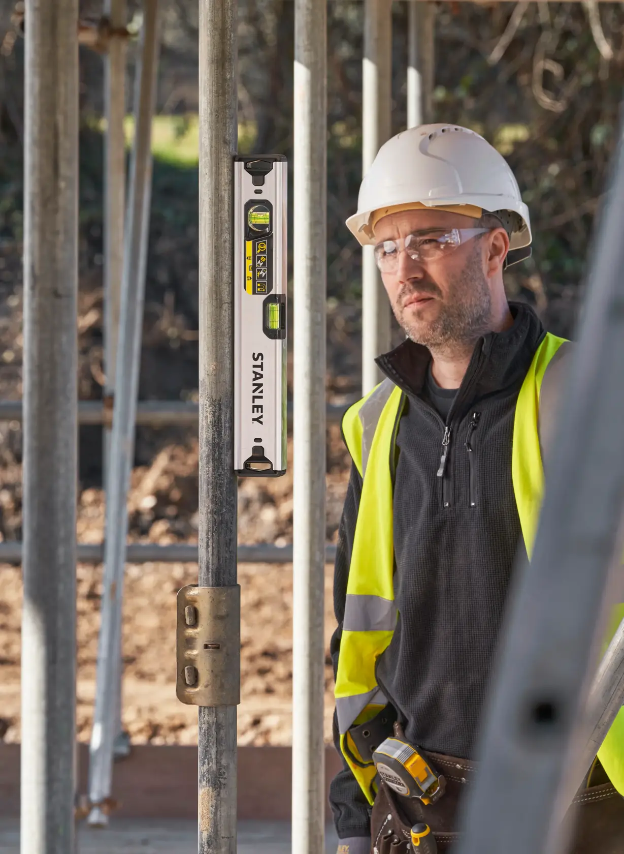 Photo of STANLEY FMHT43671-1 spirit level on metal scaffolding, construction worker in safety gear in background.