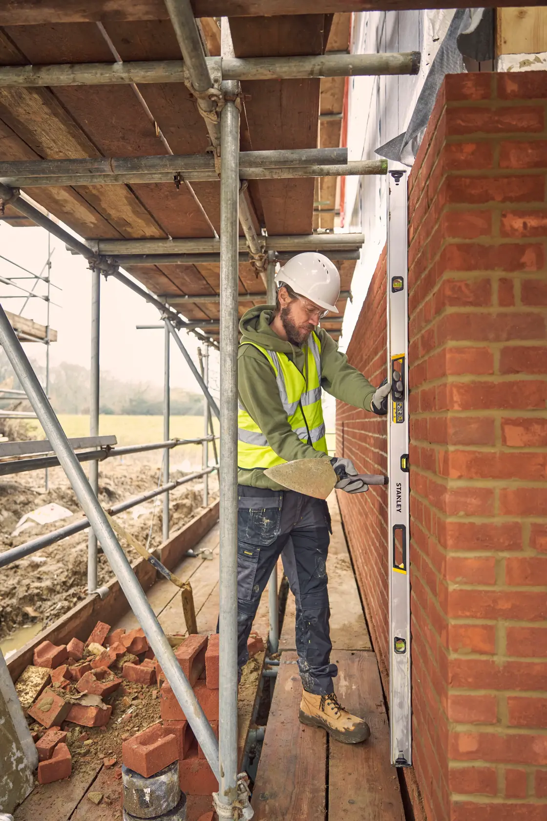 STANLEY FMHT43678-1 spirit level in use by worker checking vertical alignment of brick wall on construction site.
