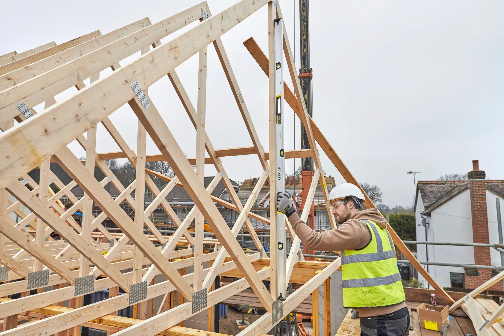 STANLEY FMHT43680-1 spirit level used by worker measuring wooden roof frames at construction site.