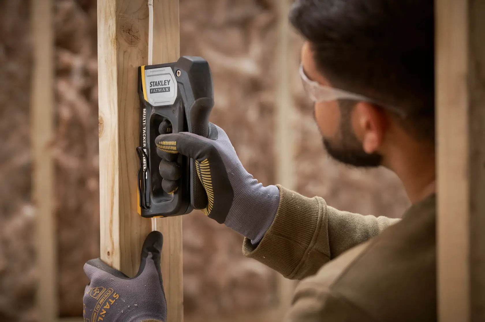 STANLEY FMHT70401-0 stapler used by gloved hands to secure wire to wood frame.
