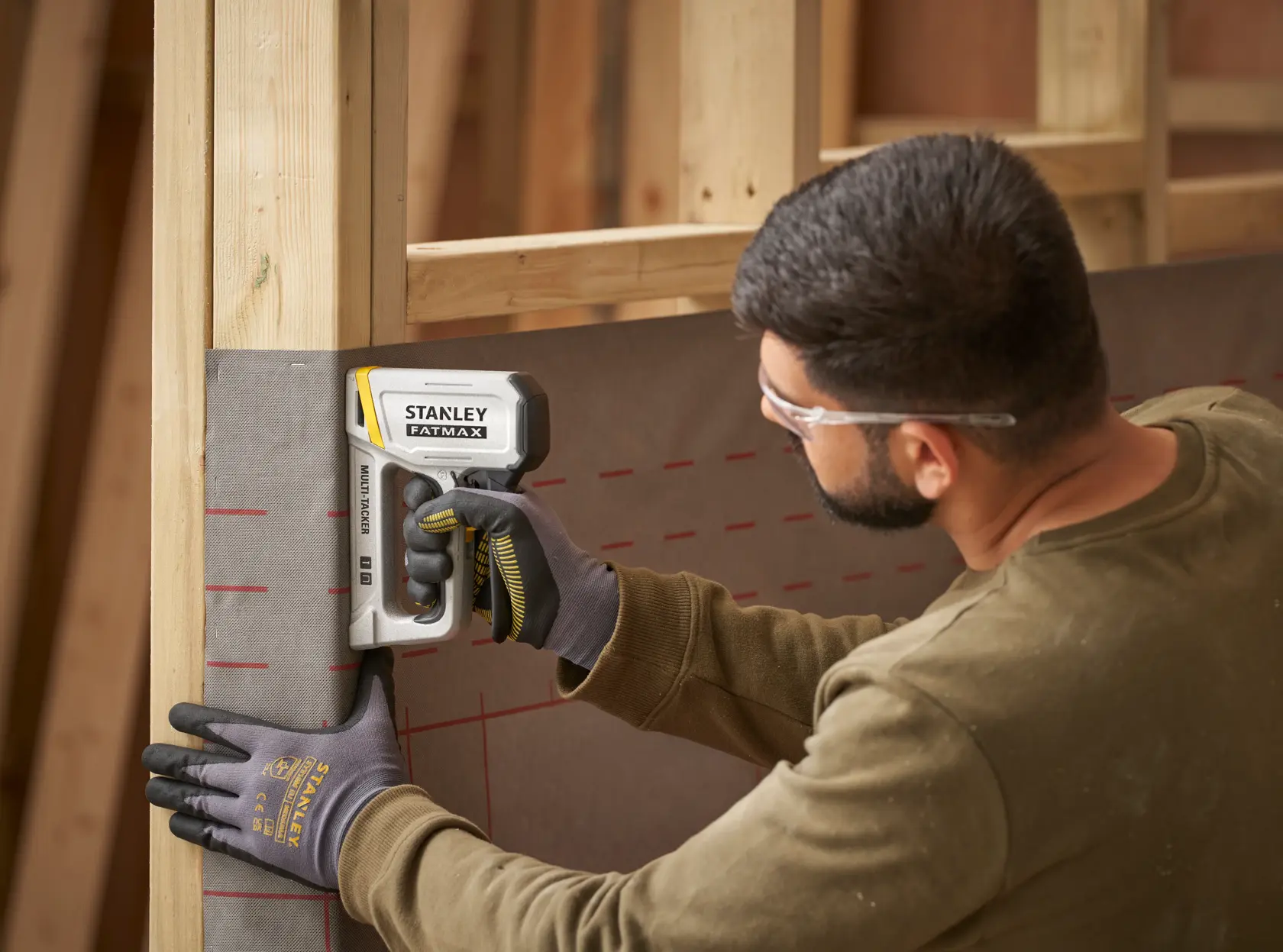 STANLEY FATMAX FMHT70443-0 stapler used by worker wearing gloves attaching sheeting to wooden frame.