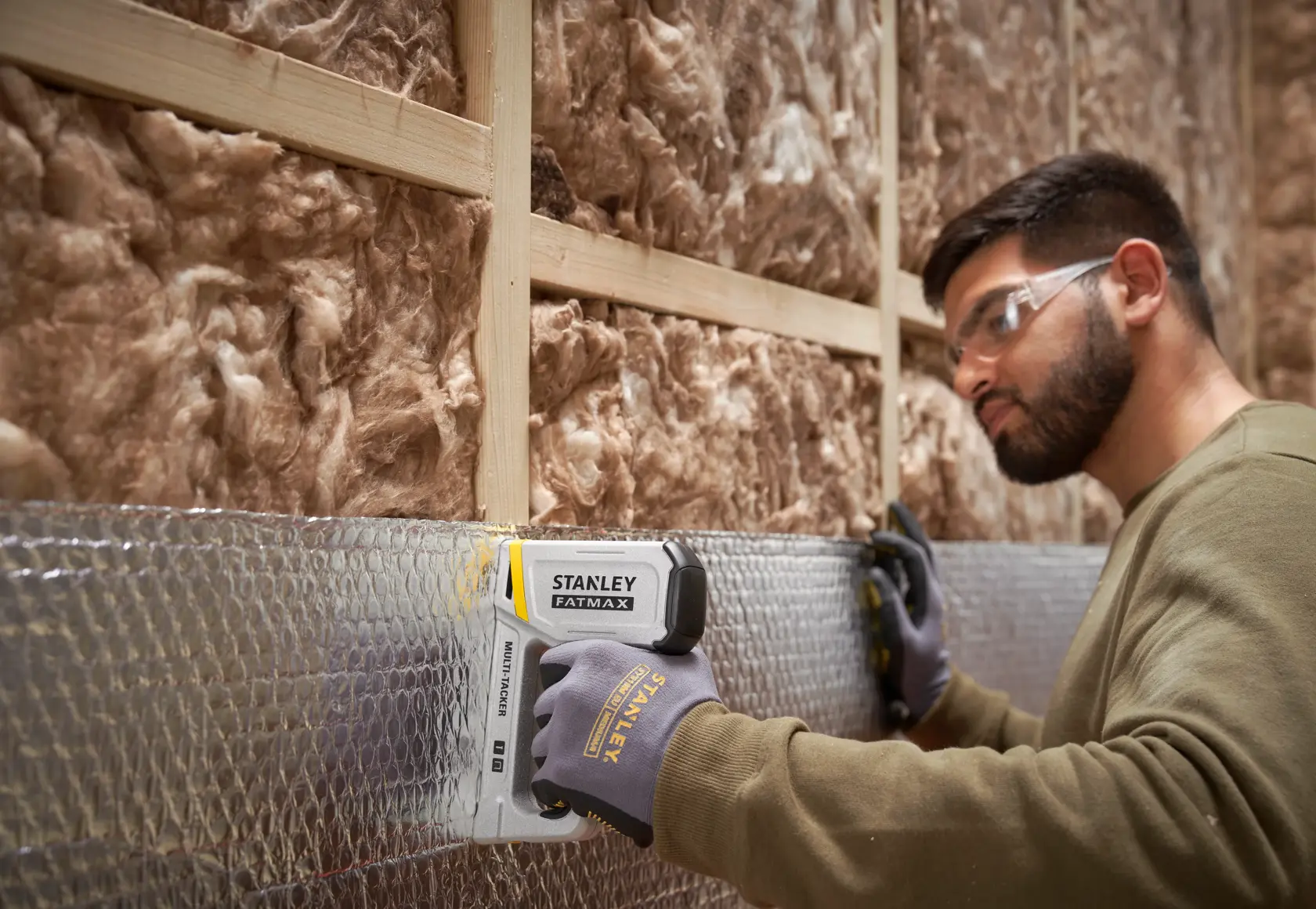 STANLEY FMHT70443-0 stapler in use, fastening insulation material to a wooden wall frame.