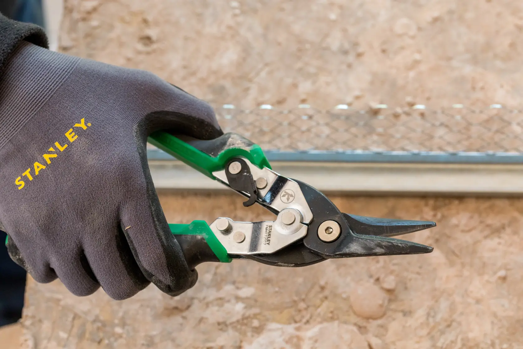 STANLEY FMHT73557-0 aviation snip with green handles held by gloved hand, close-up photo.