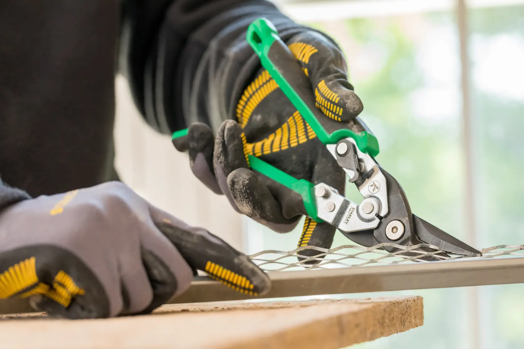 STANLEY FMHT73557-0 aviation snips with green handles cutting metal mesh, close-up in use.