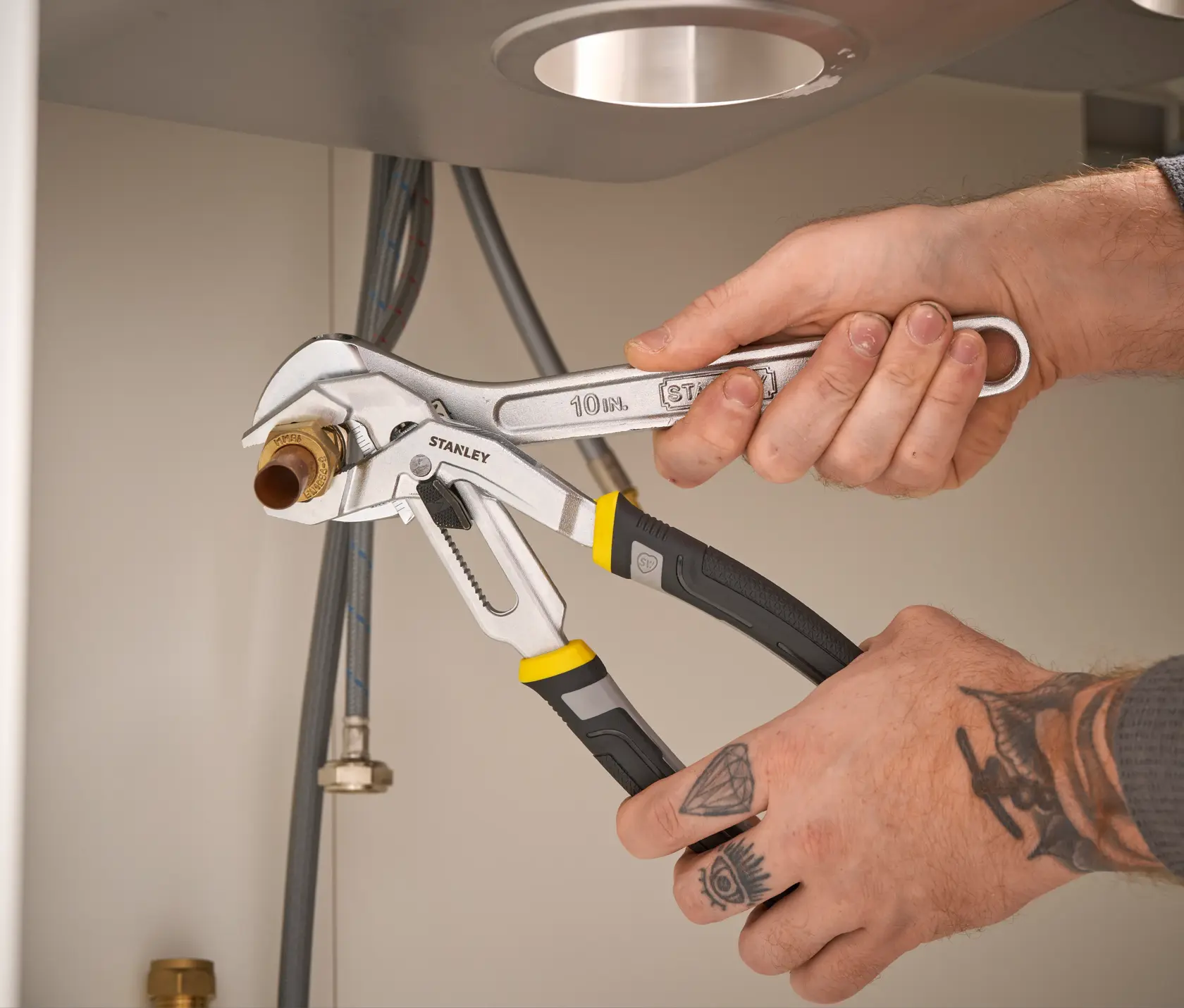 STANLEY FMHT75510-0 pince multiprise à poignées noires et jaunes utilisée pour saisir un raccord de tuyau sous un évier.