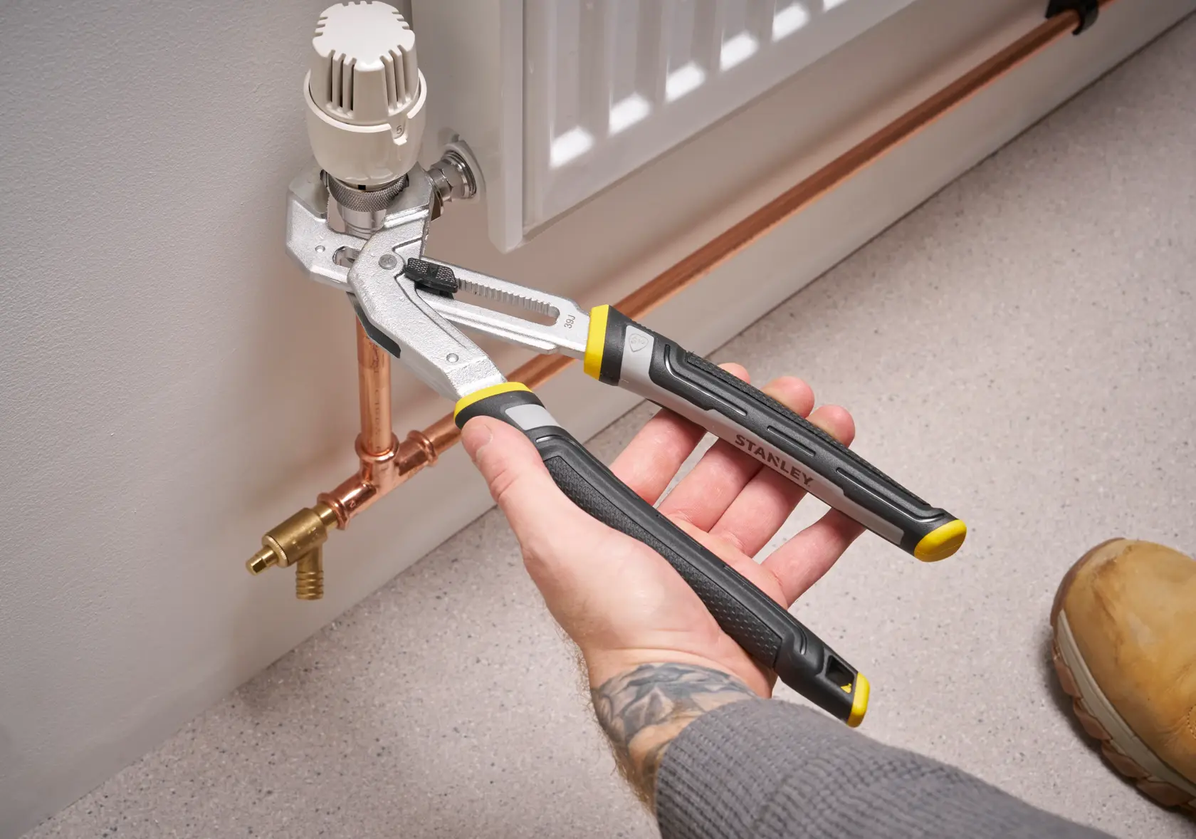 Pince réglable STANLEY FMHT75512-0 utilisée pour serrer un robinet de radiateur, montrée sur des tuyaux en cuivre.