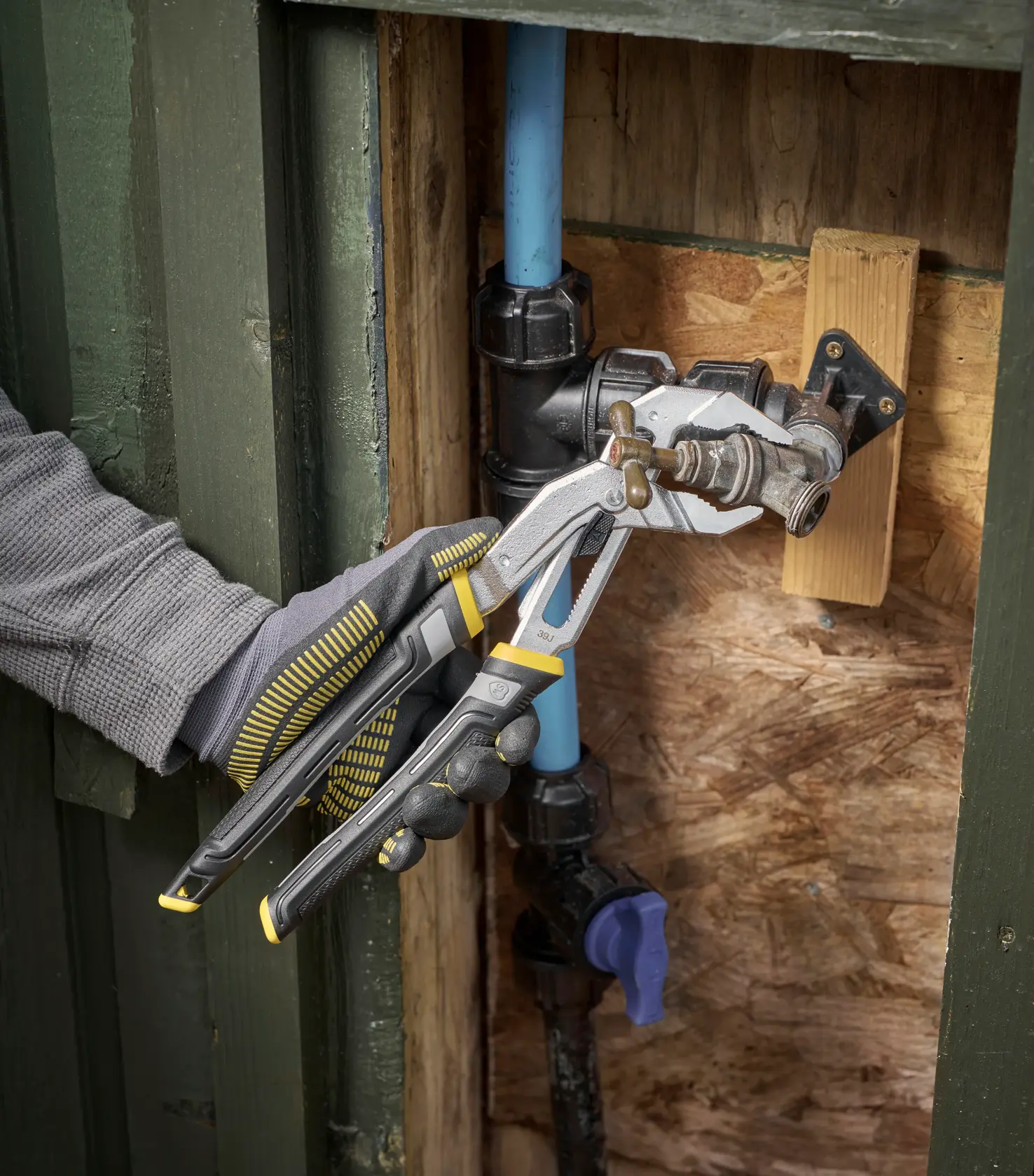 Pince multiprise STANLEY FMHT75512-0 utilisée sur un robinet extérieur, vue rapprochée, tenue avec un gant.