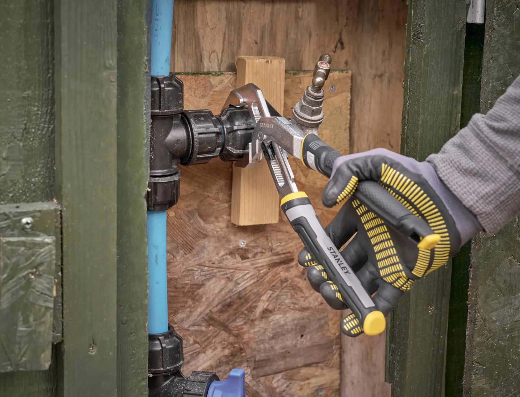 Pinces multiprises STANLEY FMHT75512-0 serrant un raccord de plomberie, utilisées en extérieur avec un gant.