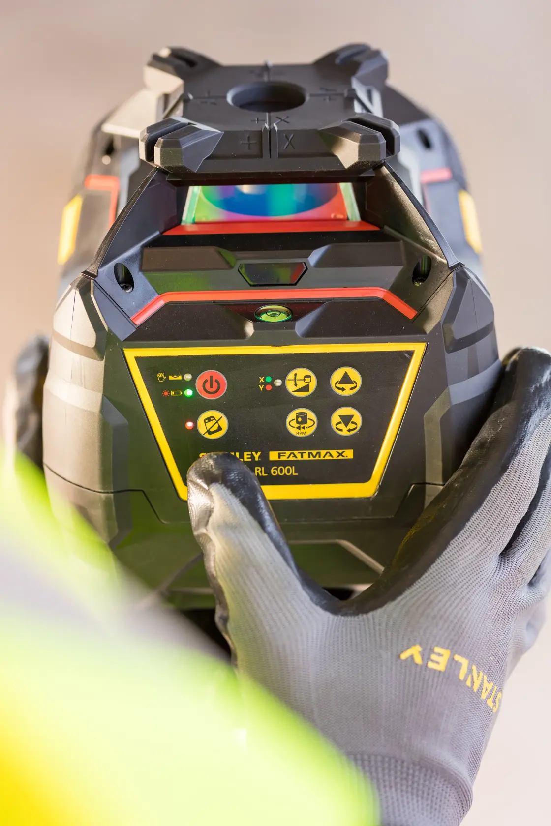 Photo of STANLEY FMHT77449-1 rotary laser level held by gloved hands, close-up of control panel.