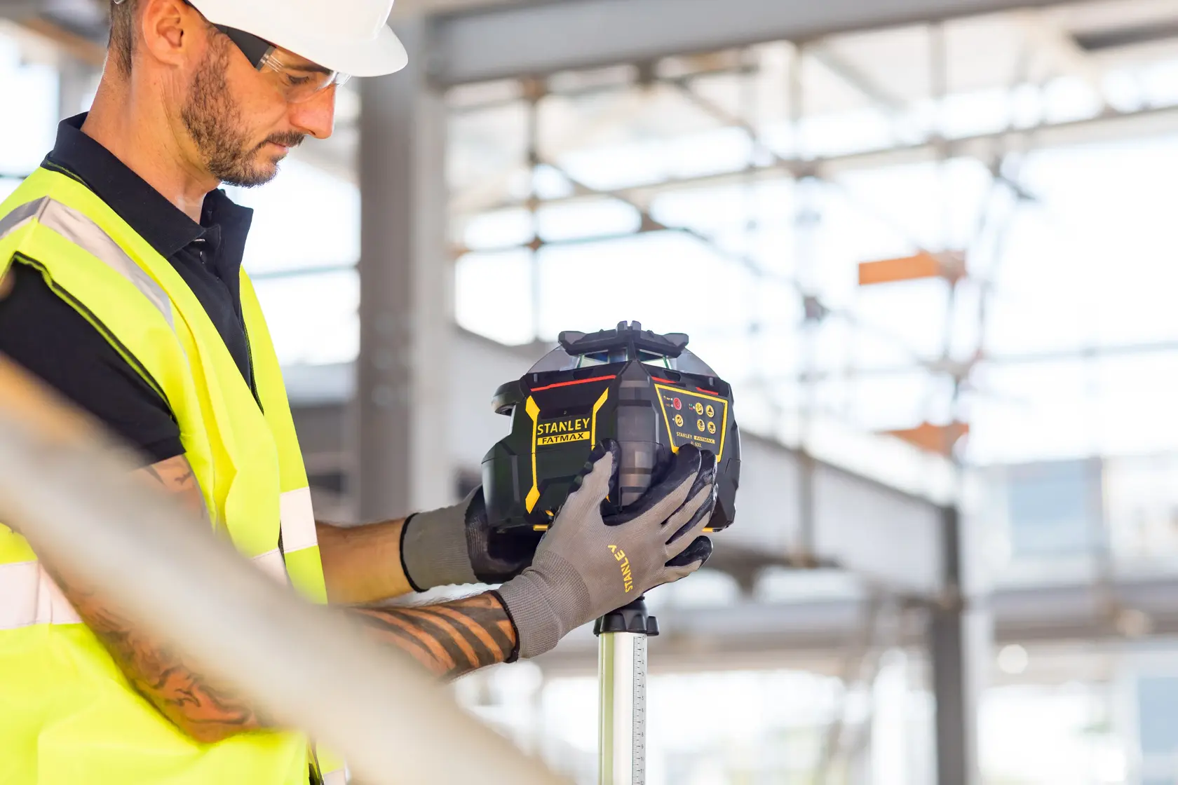 STANLEY FMHT77449-1 laser level held by worker in high-visibility vest at construction site.