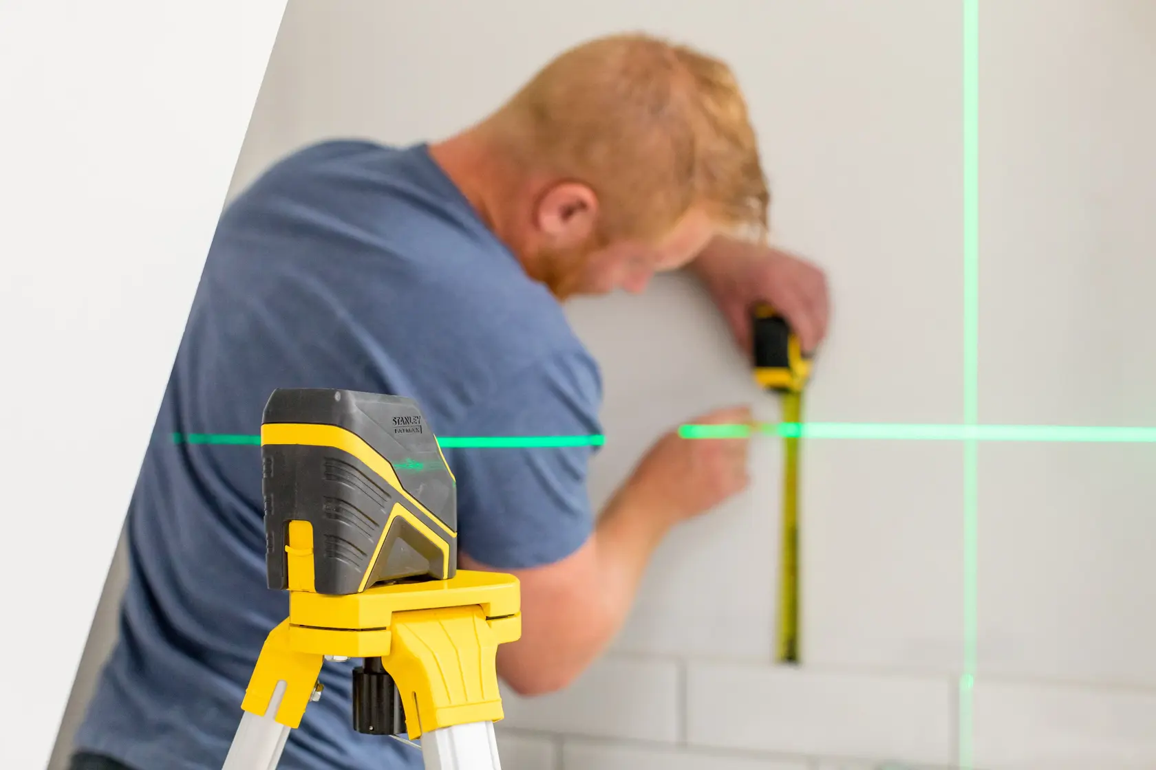 STANLEY FMHT77586-1 niveau laser sur trépied projetant des lignes vertes, personne mesurant le mur.