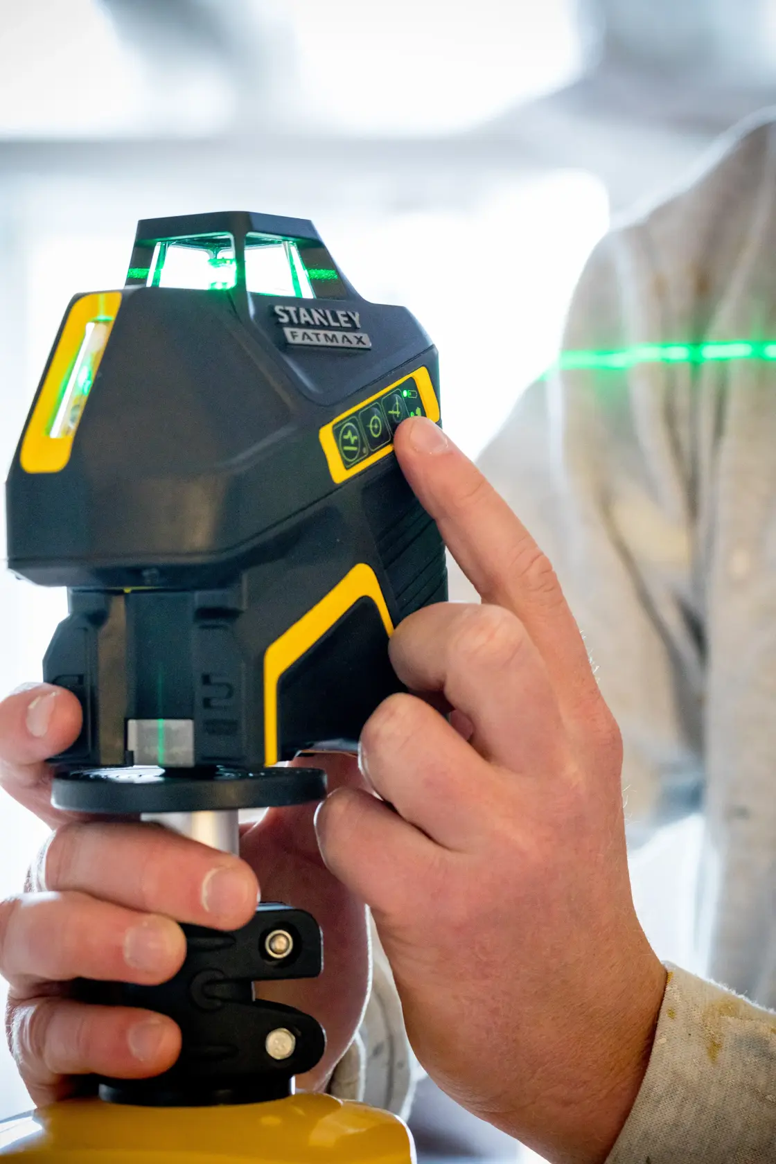 Photo of STANLEY FMHT77617-1 laser level being operated by a hand, showing illuminated control panel and green laser line.