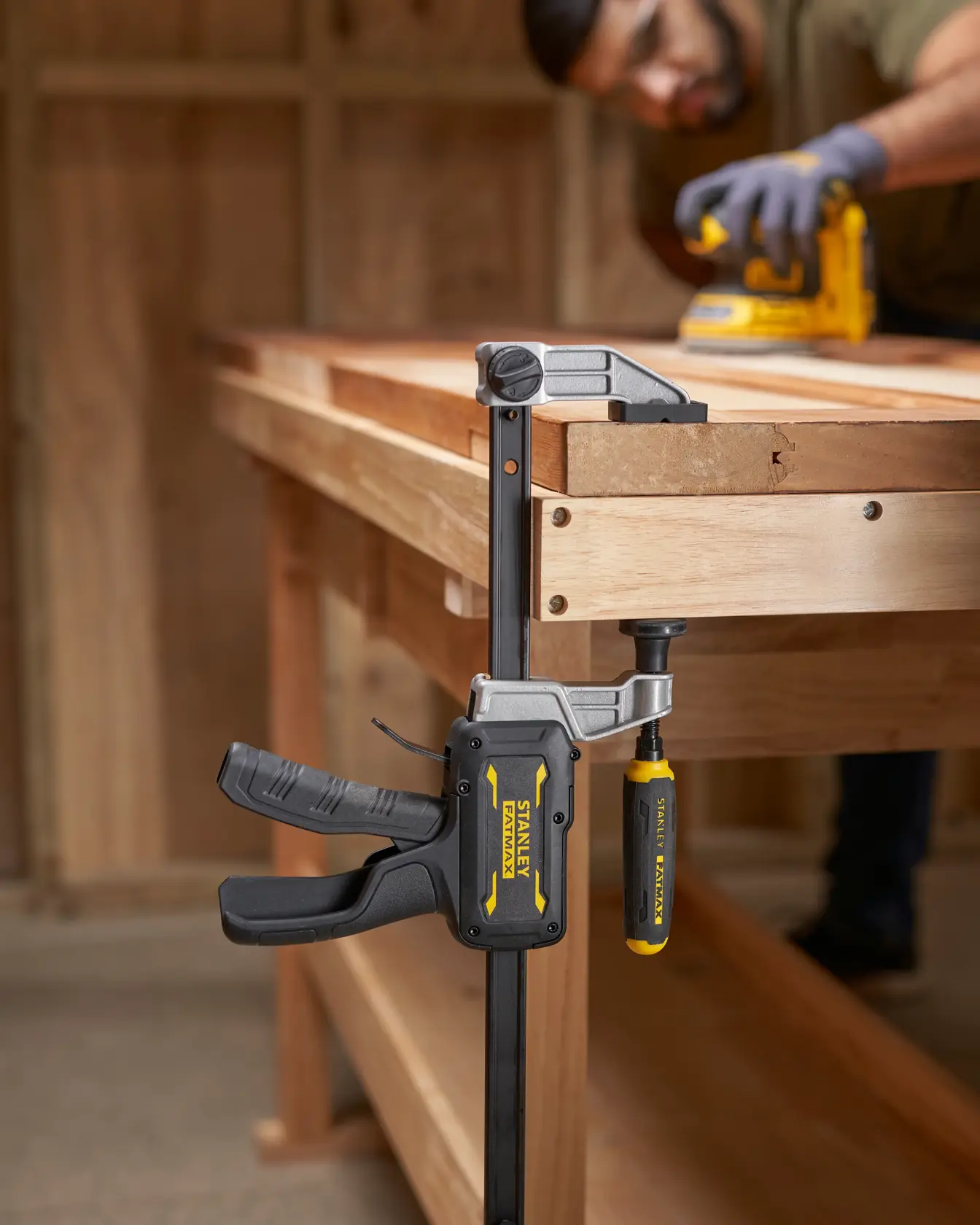 Photo of STANLEY FMHT83007-0 bar clamp attached to a wooden workbench in a workshop setting.