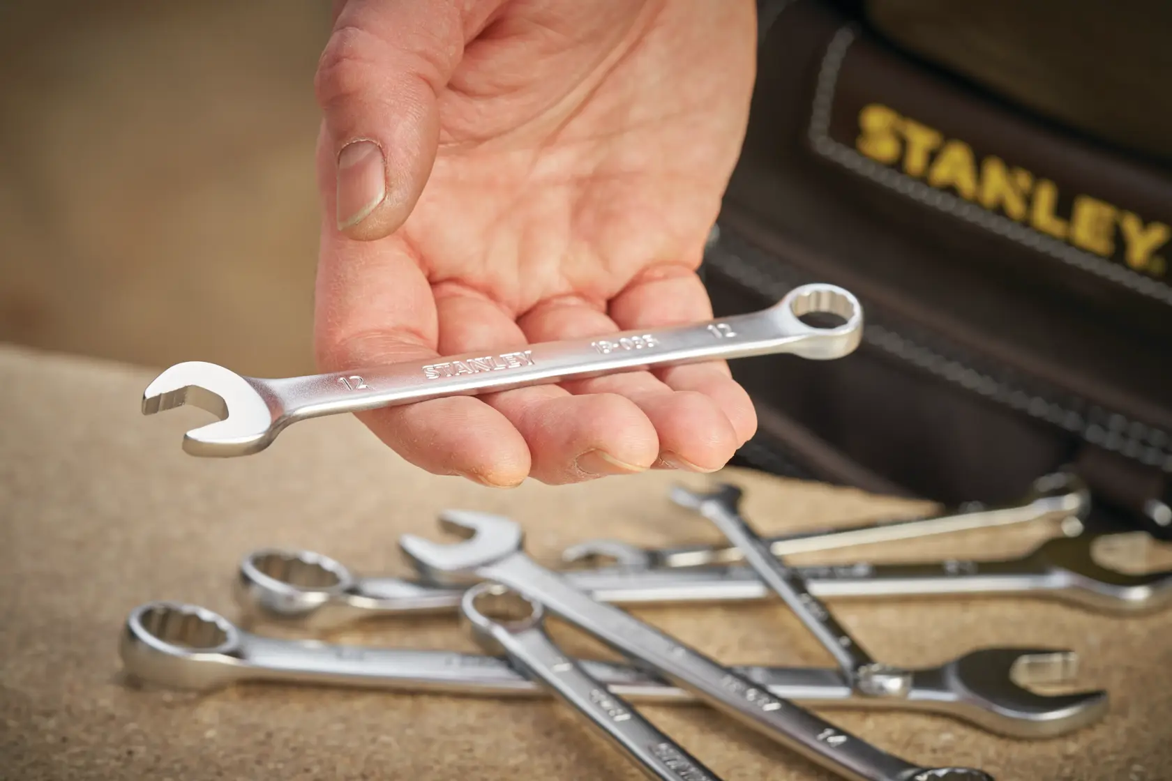 STANLEY FMMT13042-0 combination wrench held in hand, several wrenches on table, close-up photography.
