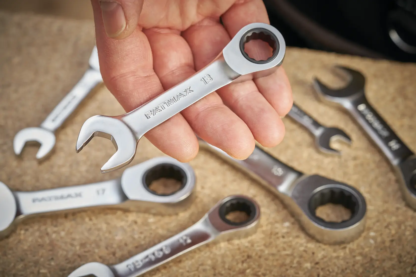 STANLEY FMMT13115-0 ratcheting combination wrench held in hand with other wrenches on a work surface.