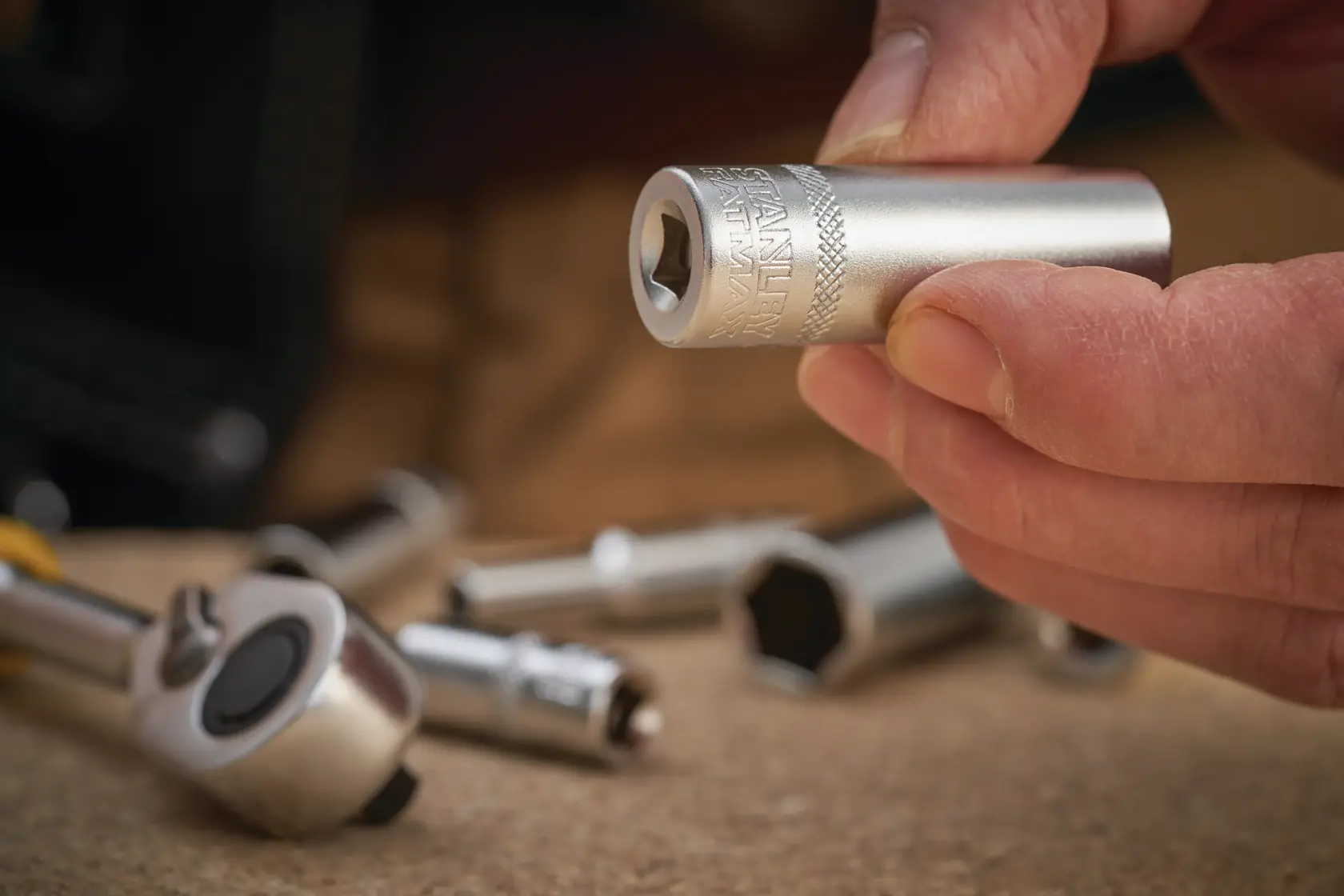 Photo of STANLEY FMMT17965-0 socket held in hand, silver color, with ratchet and sockets in background.
