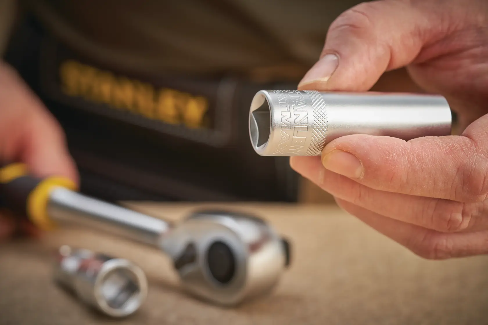 Photo of STANLEY FMMT17968-0 socket in hand, with ratchet and other sockets on workbench.