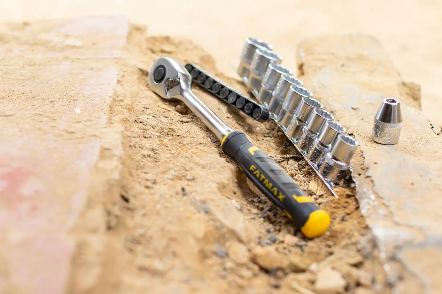 Set cricchetto e bussole STANLEY FMMT82680-0 con manico giallo e nero su terreno sabbioso, vista frontale.