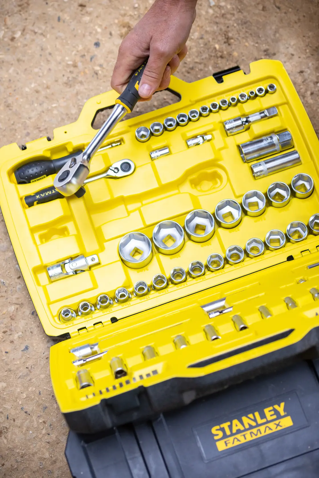 STANLEY FMMT82827-1 socket and ratchet set in yellow and black case, with hand holding ratchet, outdoor setting.