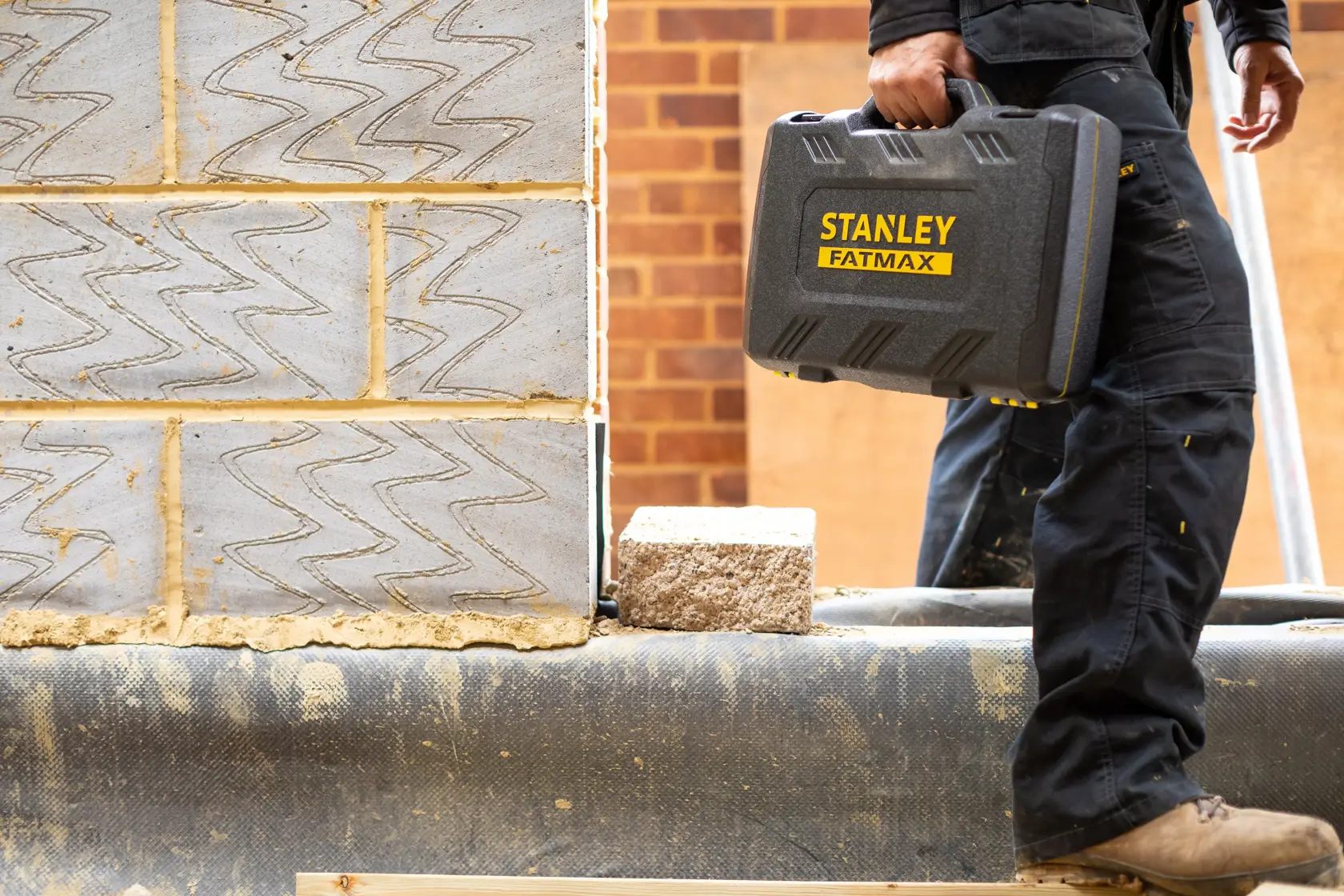 Photo of a worker carrying a STANLEY FATMAX FMMT82827-1 tool case at a construction site.
