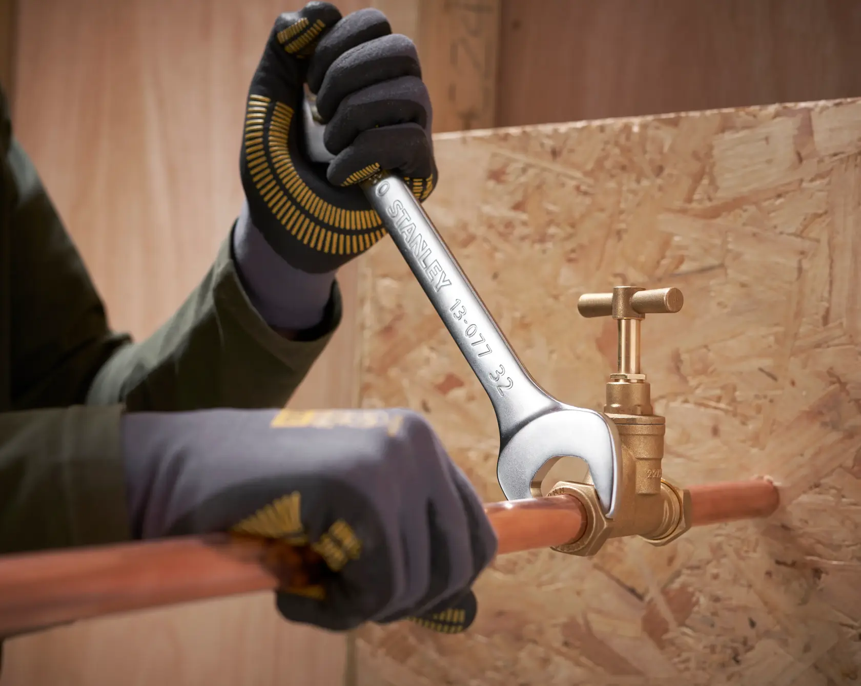 Photo of STANLEY FMMT82902-0 wrench tightening a brass valve on copper pipe, worker wearing gloves.