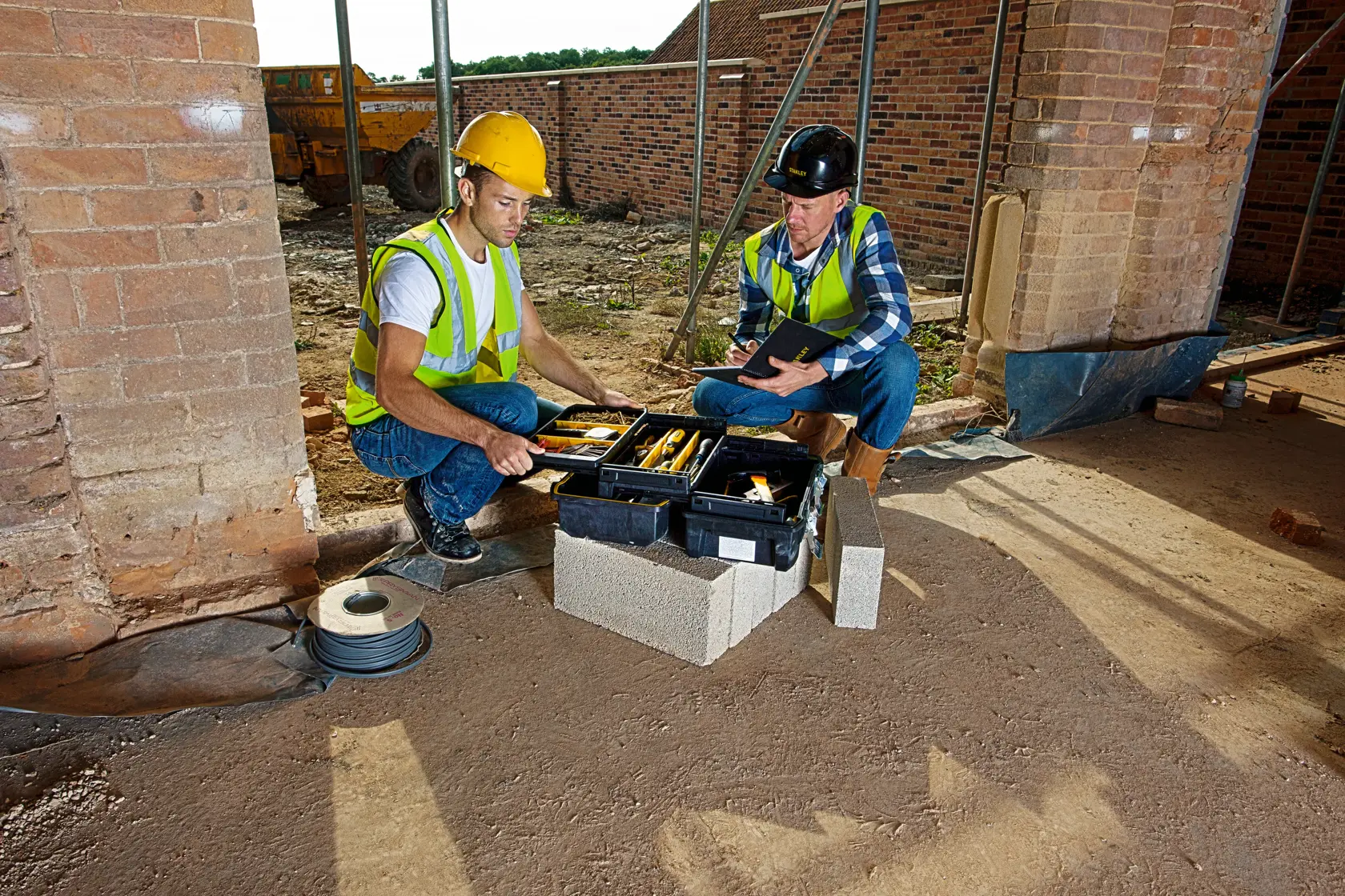 STANLEY FMST1-71219 boîte à outils sur chantier, deux ouvriers inspectent les outils, photographie produit.