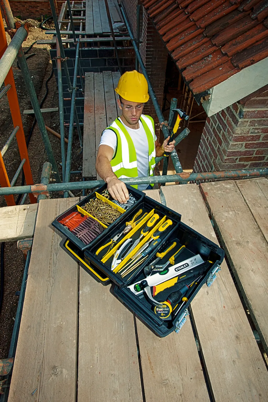 Photo de la boîte à outils STANLEY FMST1-71219 avec outils sur un échafaudage, ouvrier à proximité.