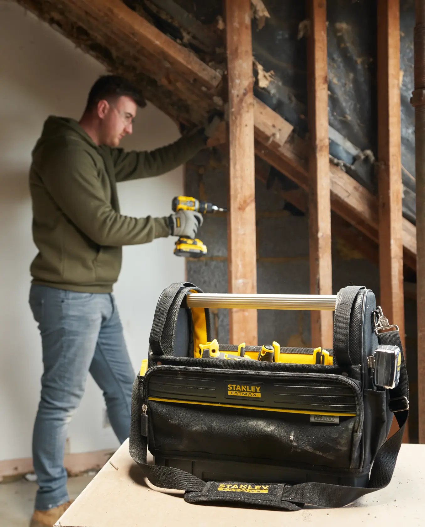 STANLEY FMST17626-1 tool bag with yellow accents on tabletop, person working in background.