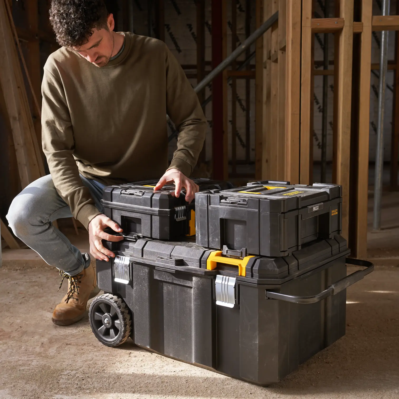 Photo of STANLEY FMST17870-1 modular black toolboxes with yellow latches and wheels, stacked at a construction site.