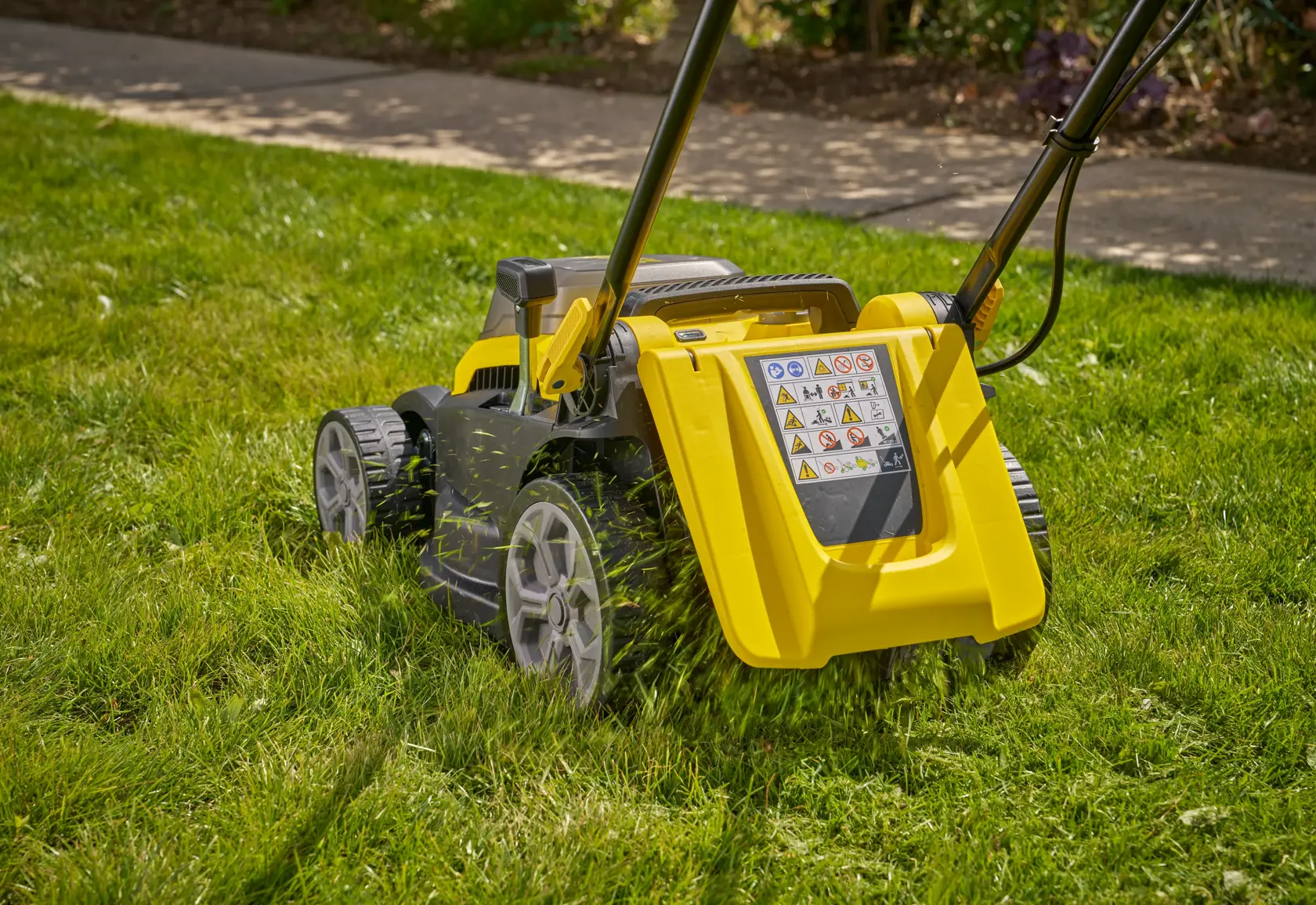 STANLEY SCMWP3401M1-XE lawn mower in yellow and black cutting grass, rear view, outdoors.