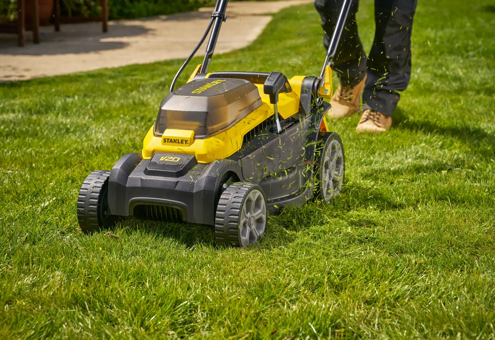 Photo of STANLEY SCMWP3401M1-XE lawn mower in use on green grass, with grass clippings visibly flying.
