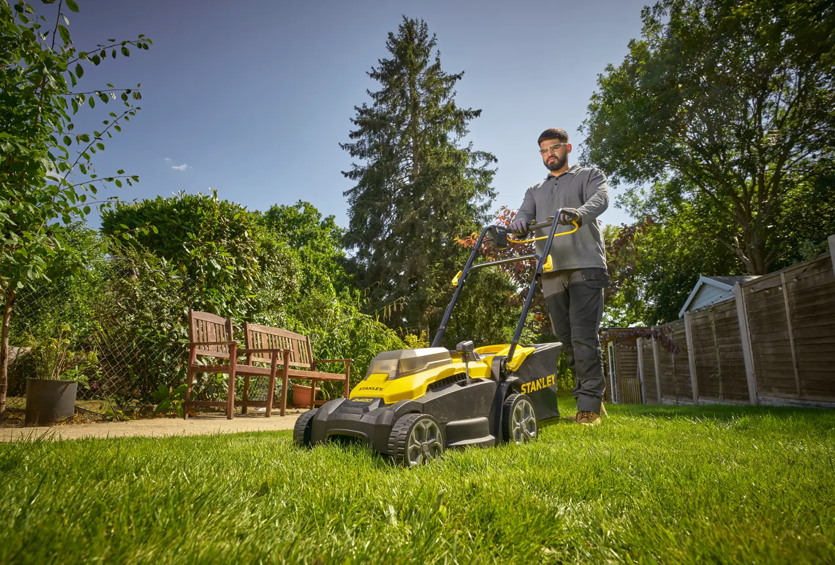 Tondeuse STANLEY SCMWP3701N utilisée sur l’herbe dans un jardin, personne poussant la tondeuse, photo en extérieur.