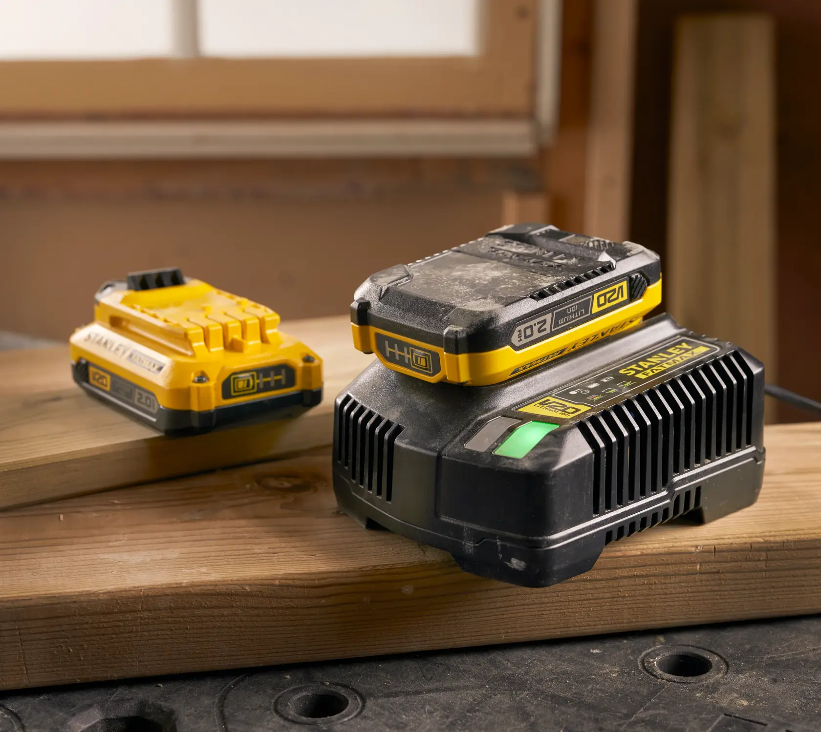 Photographie du set batterie et chargeur jaune 20V STANLEY SFMCB12D2 posés sur des planches en atelier.