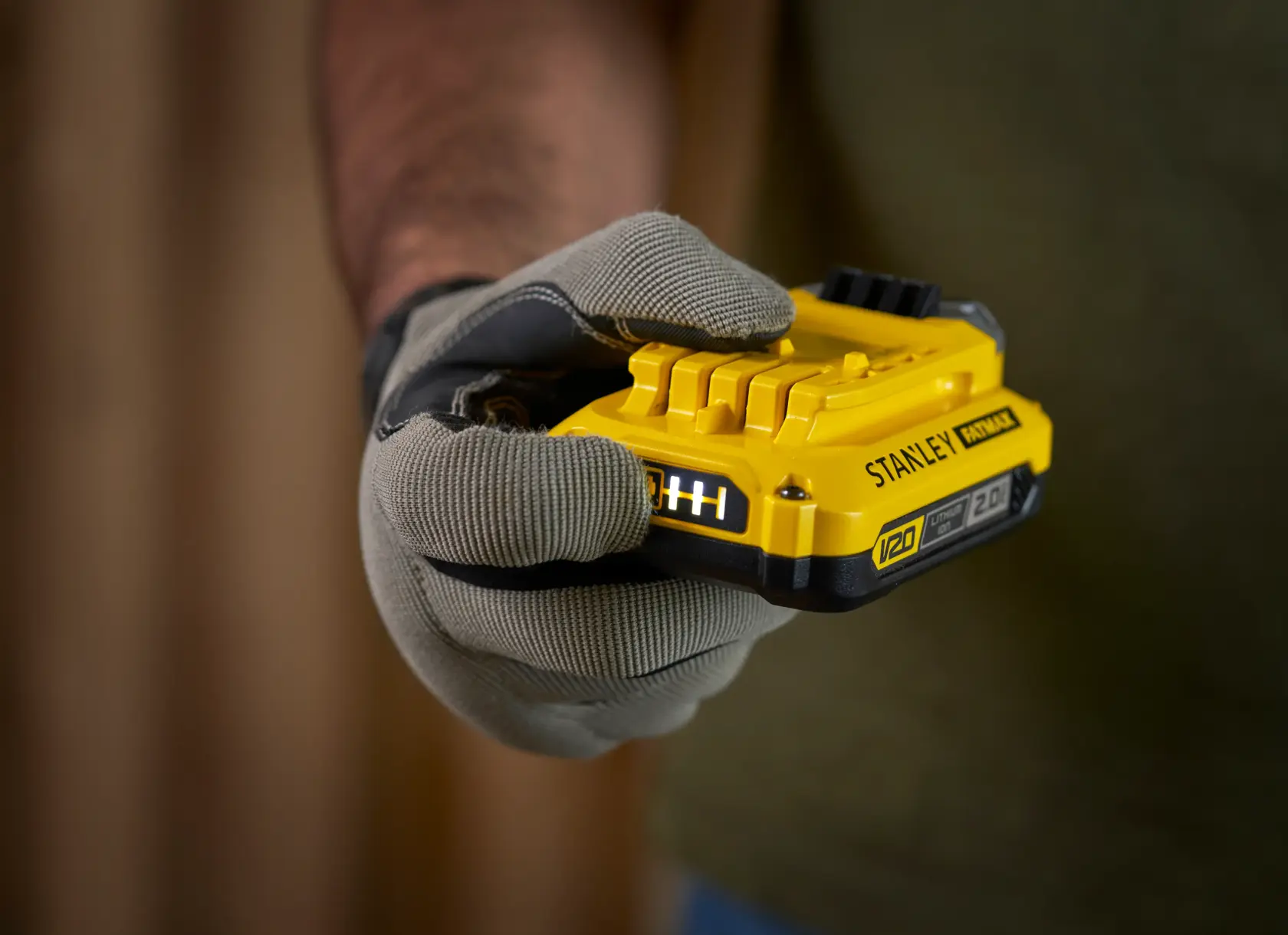 Photo of STANLEY SFMCB12D2 yellow V20 battery held in gloved hand, product photography close-up.