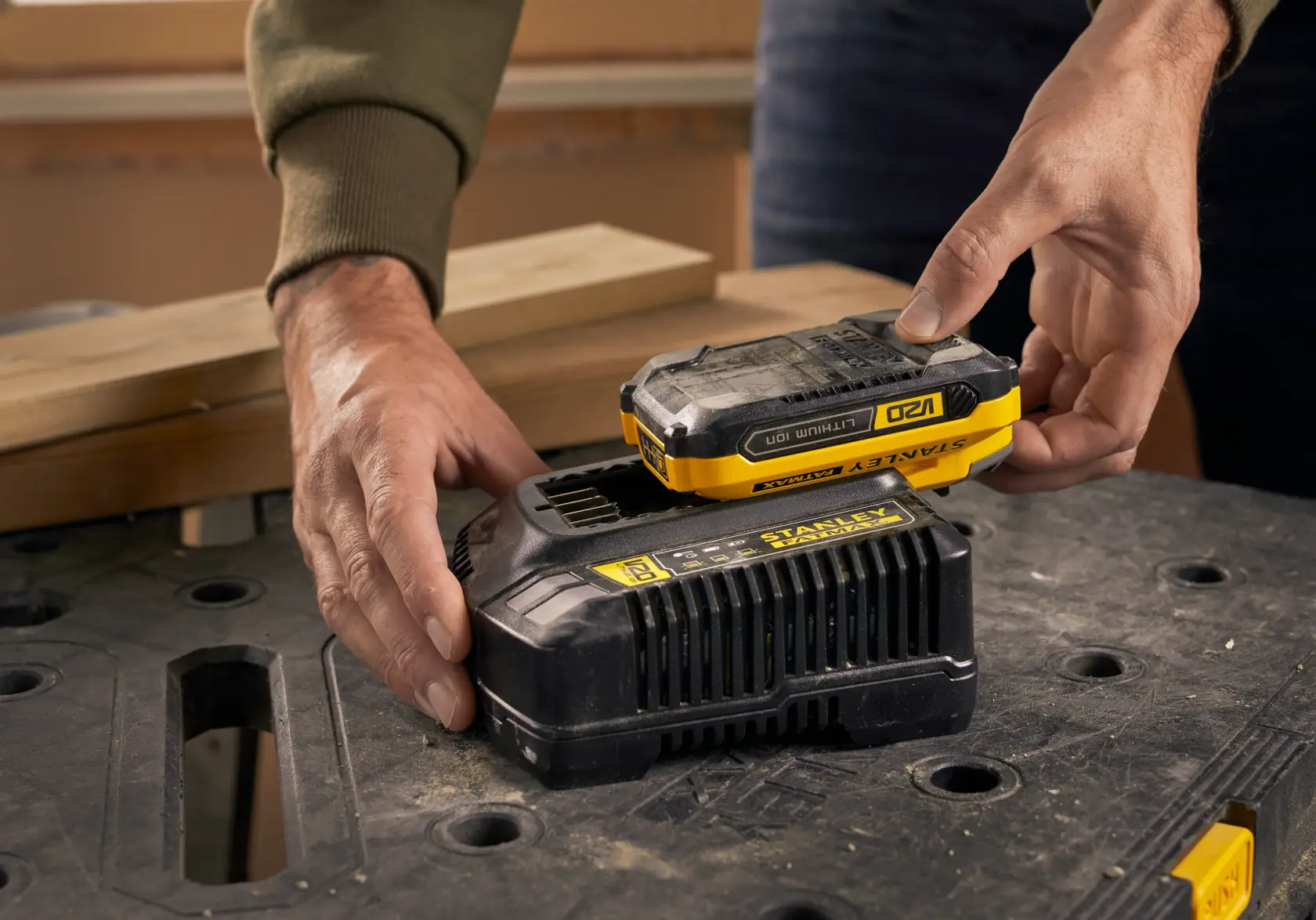 Foto del caricabatteria STANLEY SFMCB14 con batteria su banco da lavoro, mani posizionano la batteria.