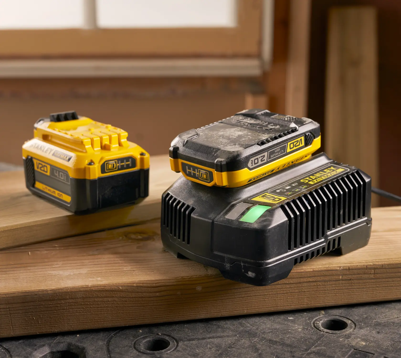 Foto della batteria e caricatore STANLEY SFMCB14 V20 agli ioni di litio su legno, sfondo officina.
