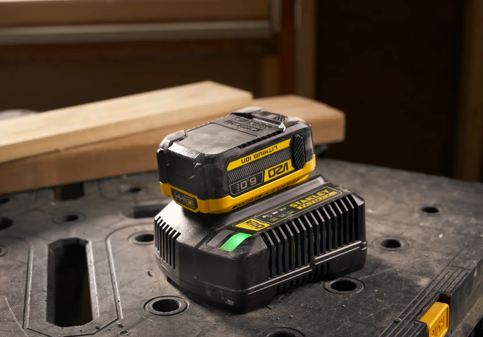 Batterie lithium-ion Stanley SFMCB206 et chargeur sur un établi, photographie prise de côté avant.