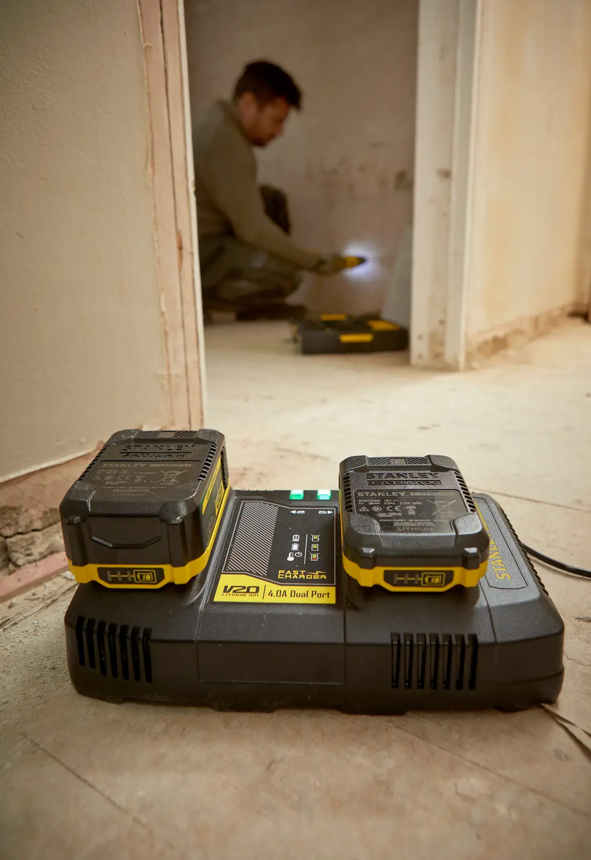 Caricabatterie doppio STANLEY SFMCB24 con due batterie V20 sul pavimento in un cantiere.