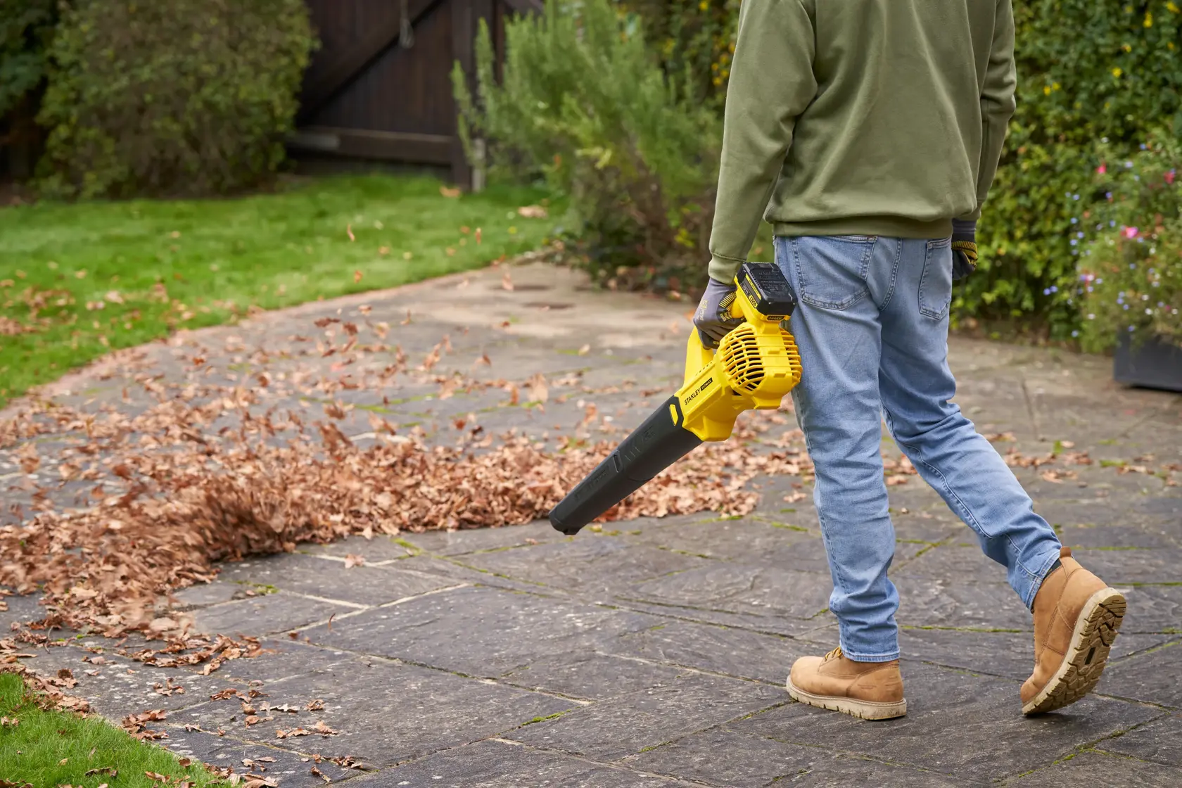 Photo d'une personne utilisant un souffleur de feuilles sans fil STANLEY SFMCBL714B-XJ sur une terrasse couverte de feuilles.
