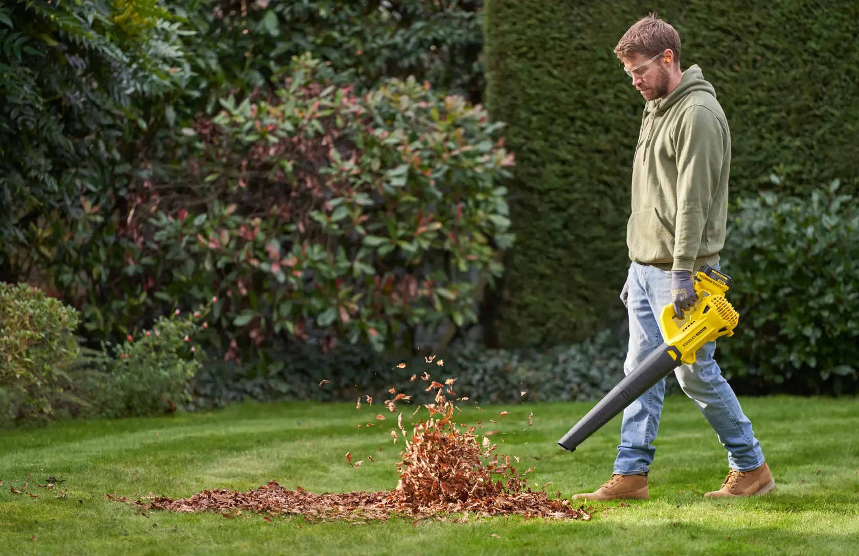 STANLEY SFMCBL714B-XJ souffleur de feuilles utilisé sur de l’herbe, déplaçant un tas de feuilles sèches dans un jardin.