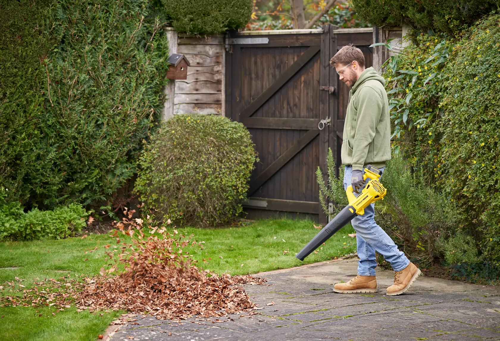 Photo d'une personne utilisant le souffleur de feuilles sans fil STANLEY SFMCBL714M1 pour nettoyer une terrasse de jardin.