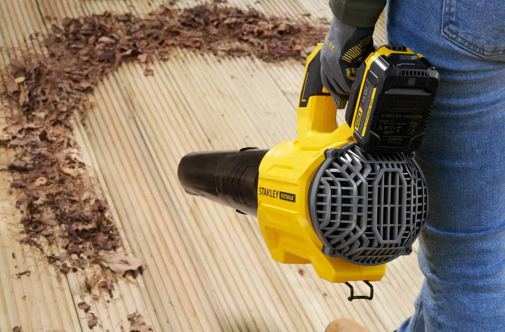STANLEY SFMCBL730B souffleur de feuilles utilisé sur terrasse en bois, enlève des feuilles sèches, vue latérale.