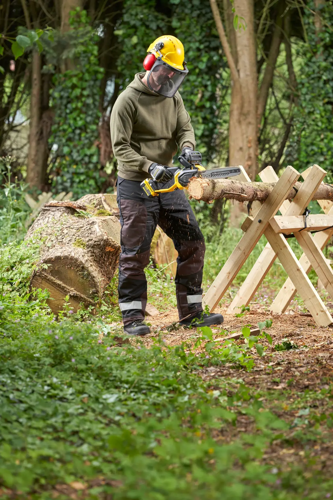 STANLEY SFMCCS730M1 chainsaw in use outdoors cutting wood, shown held by a person wearing safety gear.