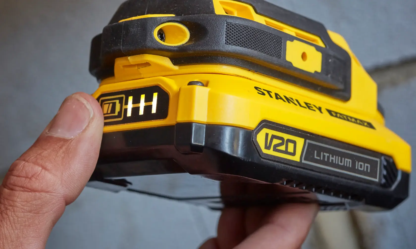Stanley SFMCD711B batterie V20 Lithium Ion en gros plan, boîtier jaune et noir, doigt sur l'indicateur.